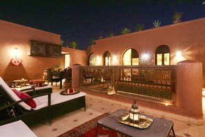 Un área de lounge al aire libre bien iluminada, con un sofá, una mesa con bandeja y un farol decorativo.