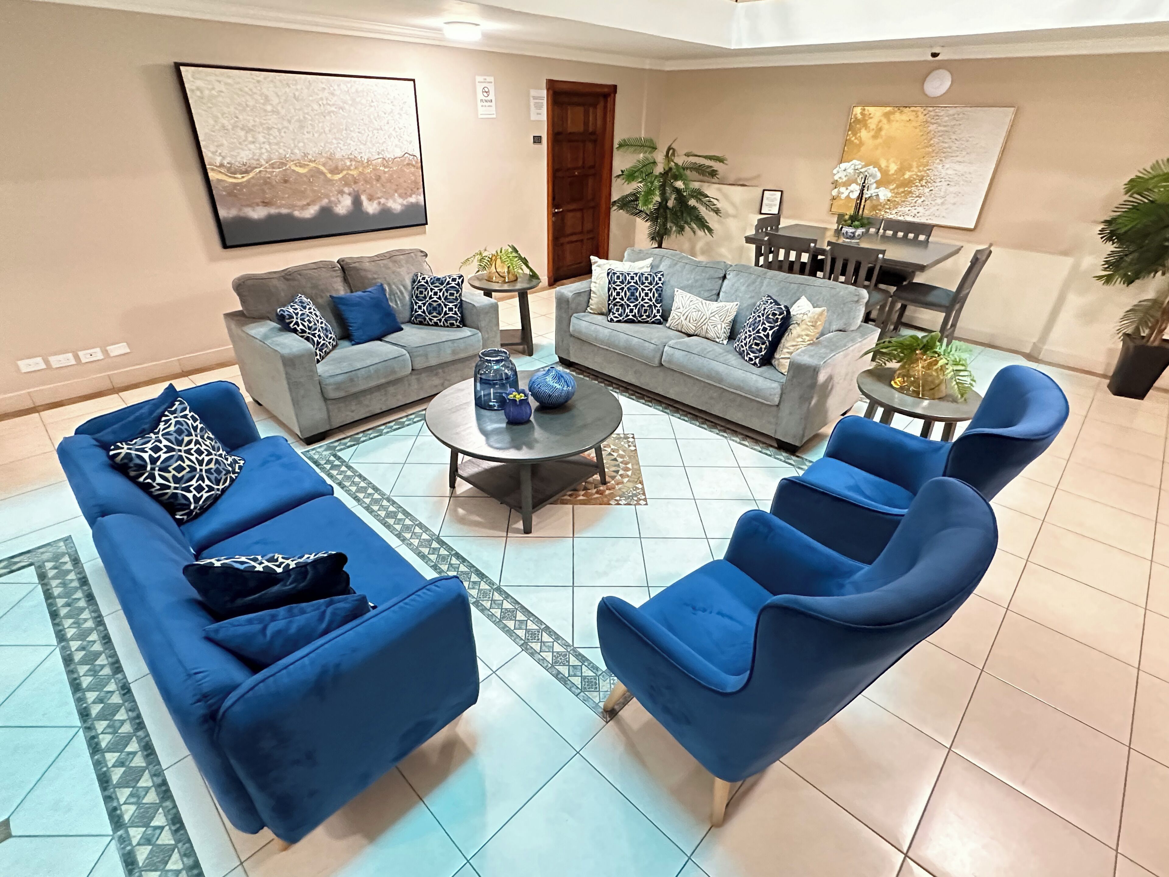 A spacious living room with two grey sofas and blue armchairs, a coffee table, and a dining area with a table and chairs.