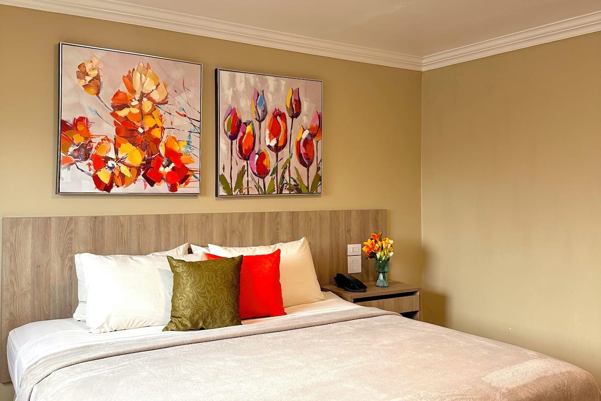 A hotel room with a large bed, a nightstand, and two wall-mounted paintings.