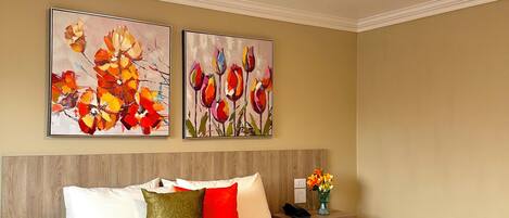 A hotel room with a large bed, a nightstand, and two wall-mounted paintings.