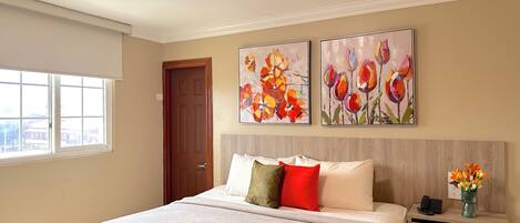 A bedroom with a bed, a nightstand, a window, and two floral paintings on the wall.