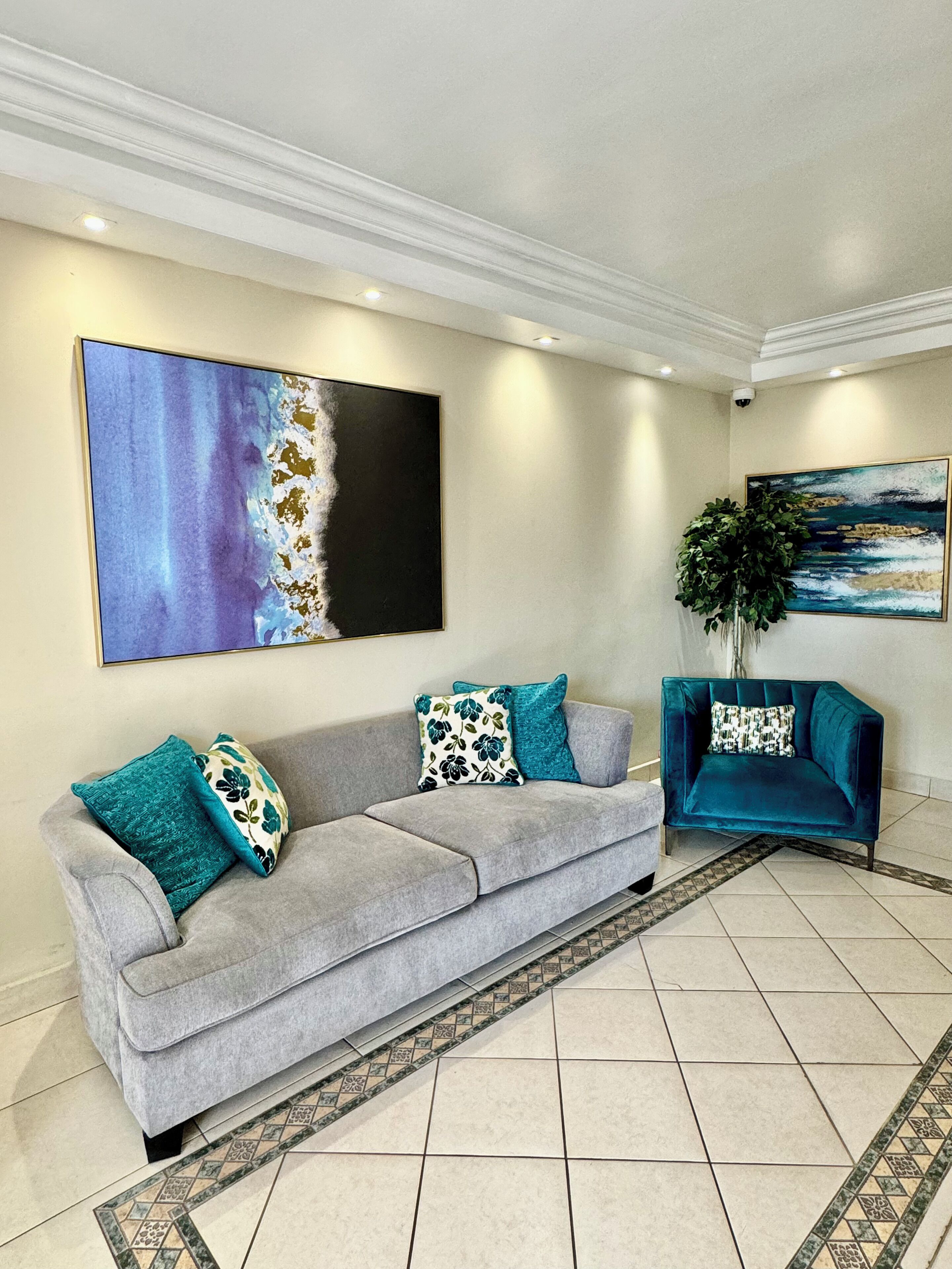 Un salón con un sofá gris, cojines color turquesa, un sillón azul y dos grandes cuadros abstractos en las paredes.