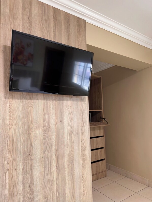 A flat-screen TV mounted on a wooden wall in a room with a tiled floor and a wooden cabinet.