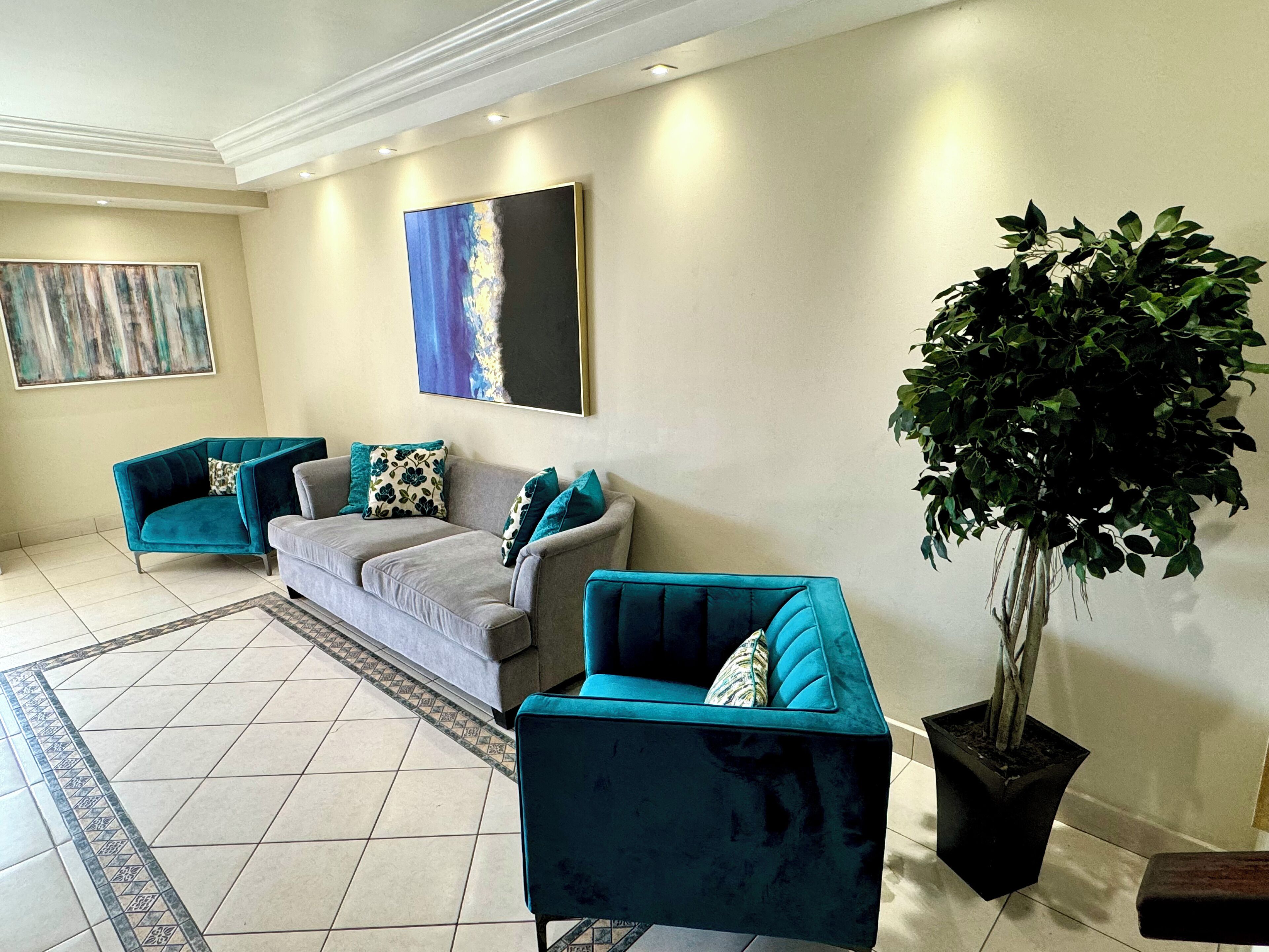 A living room with teal armchairs, a grey sofa, and a large potted plant.