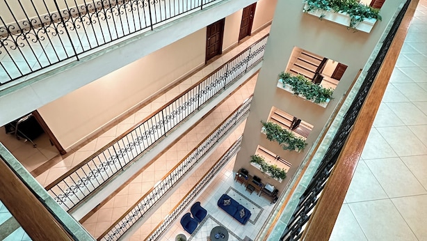 A multi-level atrium with a central open space featuring sofas and tables, surrounded by balconies with railings and potted plants. - Hotel Andros (Colon)