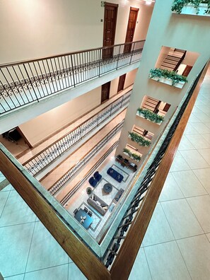 A multi-level atrium with a central open space featuring sofas and tables, surrounded by balconies with railings and potted plants.