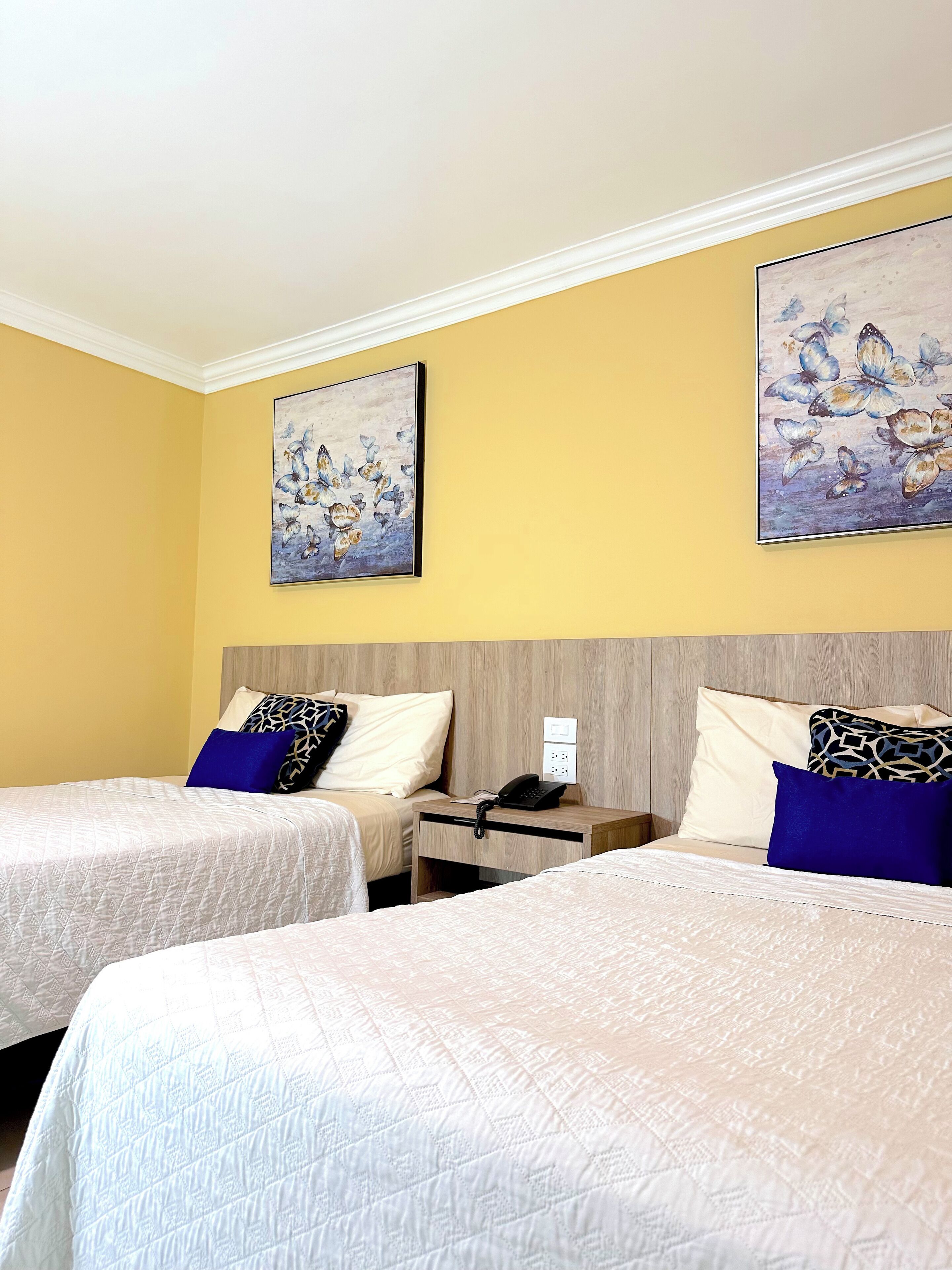 Una habitación de hotel con dos camas, una mesita de noche y dos cuadros en la pared.