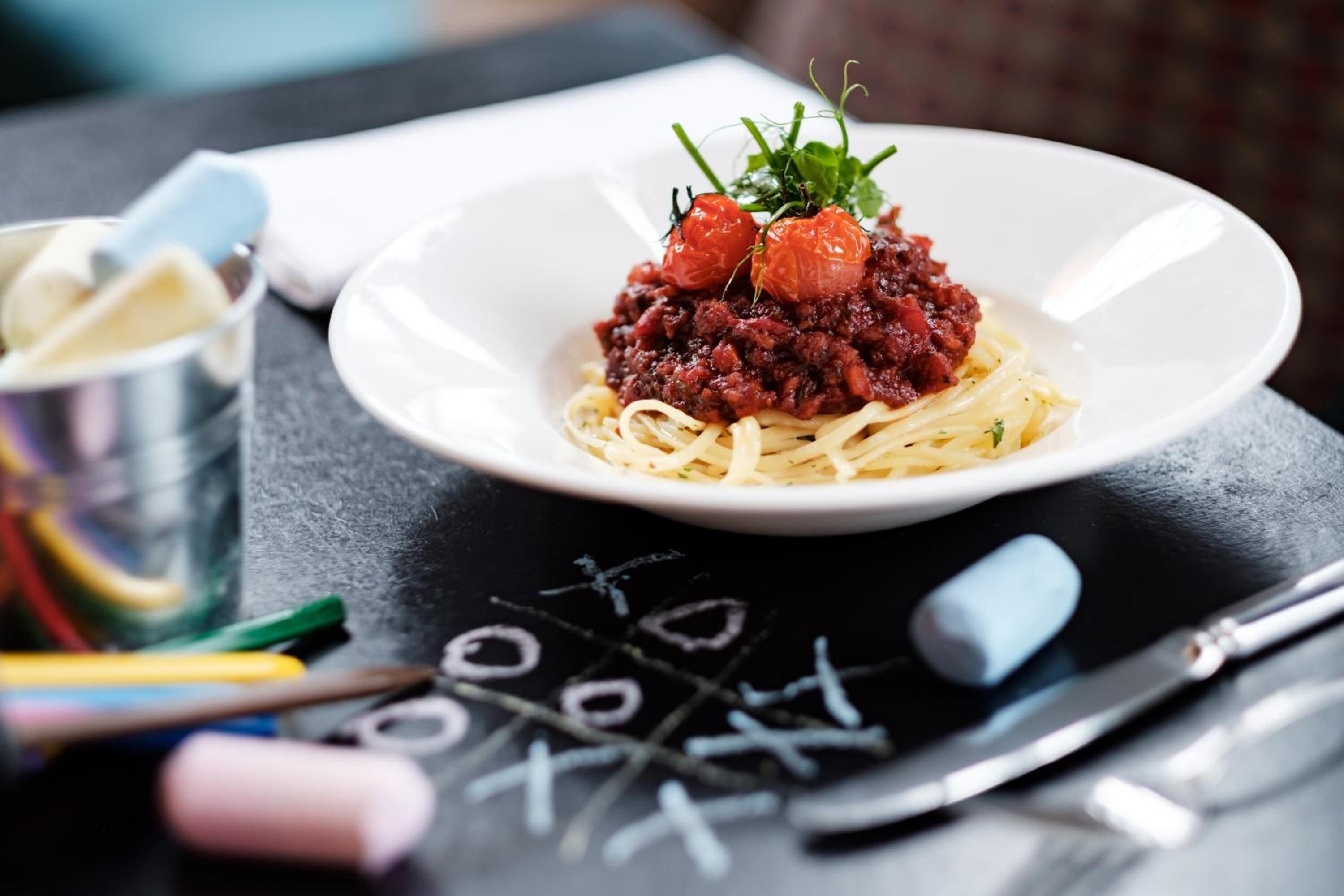 Une assiette de spaghettis nappés d’une sauce à base de viande et garnie de tomates cerises, le tout servi dans une assiette blanche.