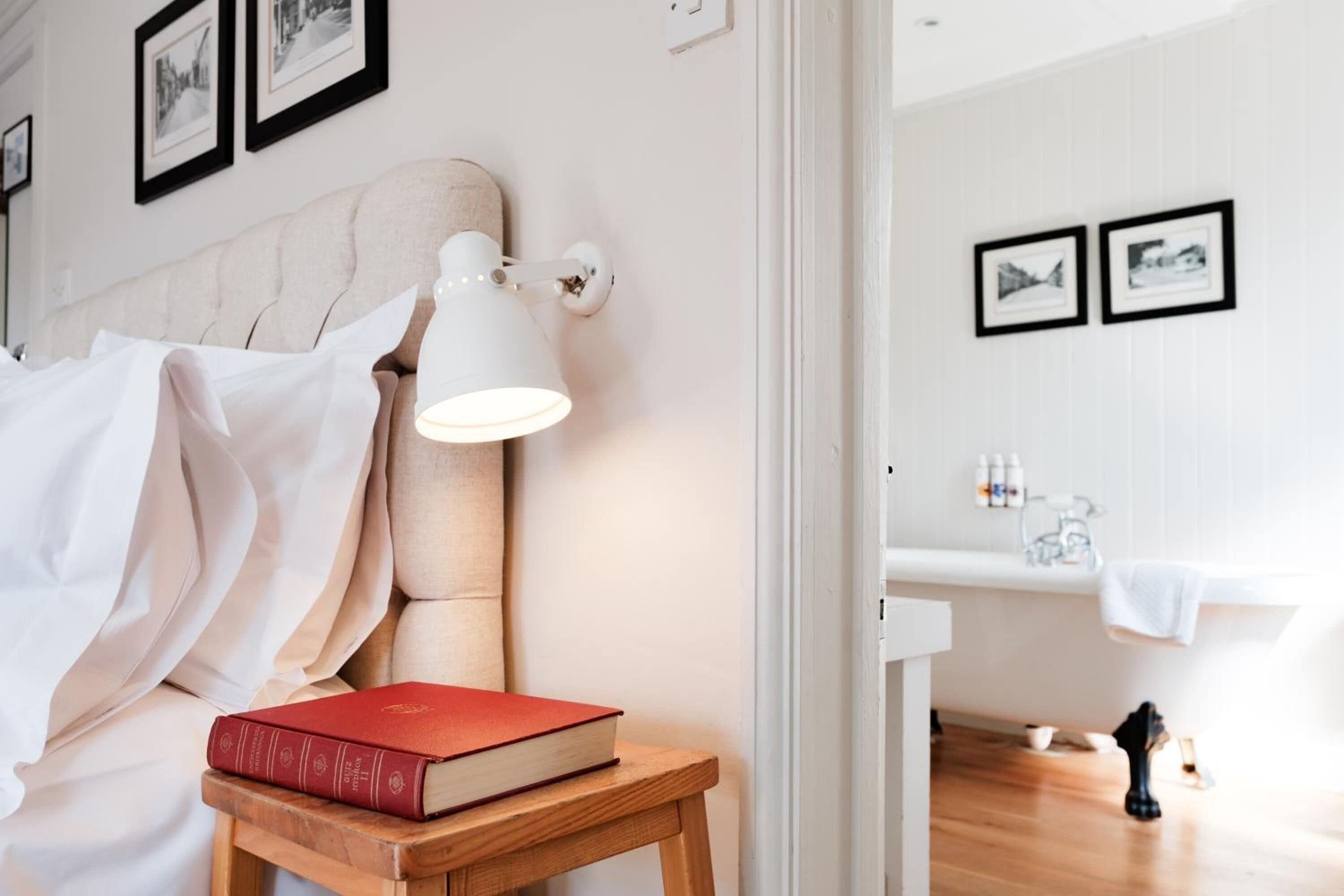 A bedroom with a bed, a bedside table with a book, a lamp, and a view into the bathroom.