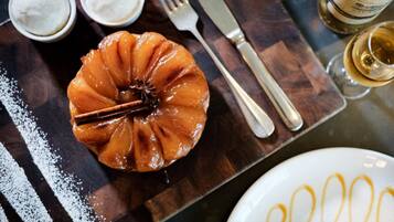 A caramel-glazed apple dessert on a wooden board, accompanied by a fork, knife, and a glass of white wine.
