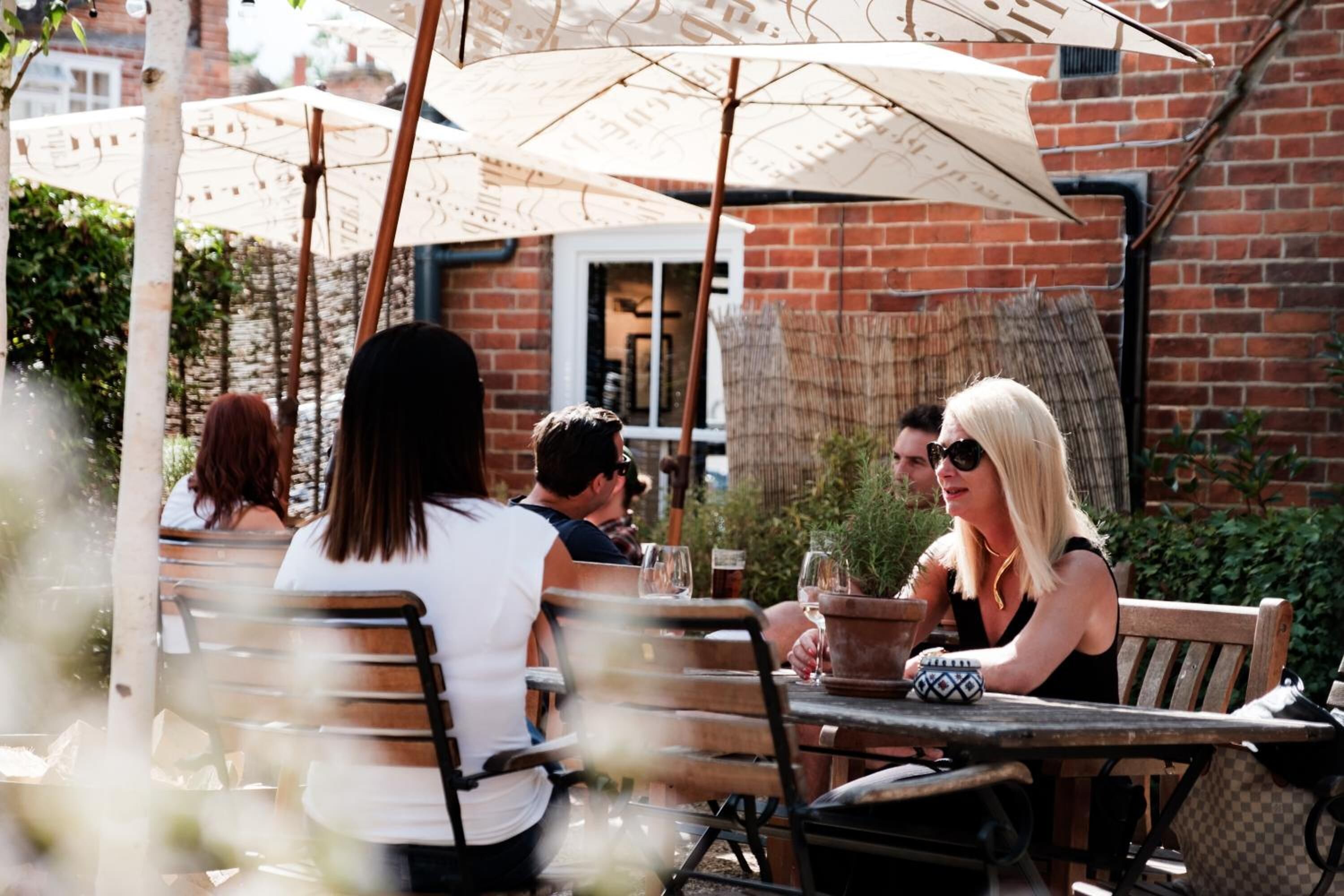 An outdoor patio with wooden tables and chairs, umbrellas, and potted plants.