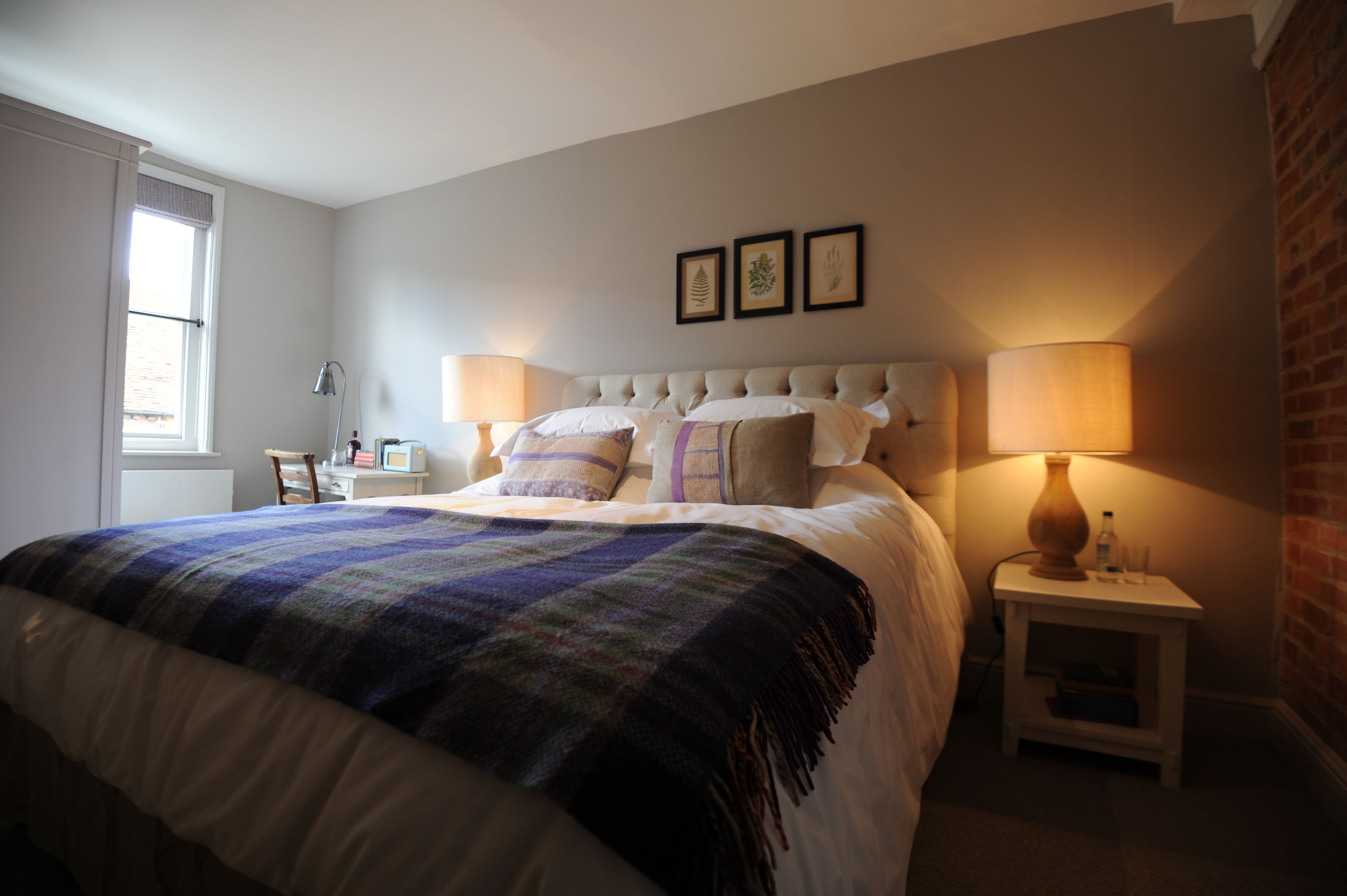 A bedroom with a large bed, two bedside tables, a window, and a brick wall.