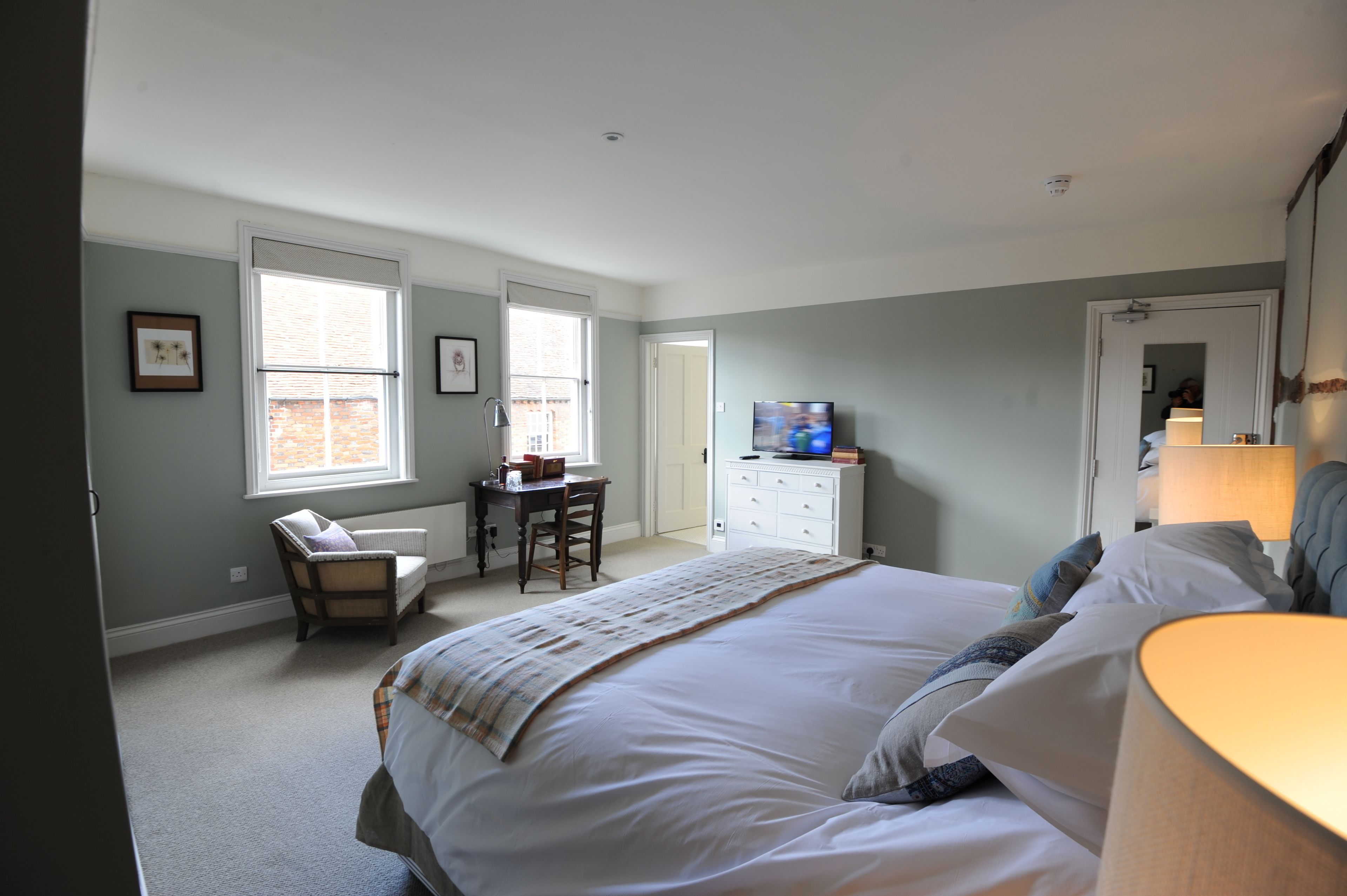 A bedroom with a large bed, a desk, a chair, a television, and a dresser.