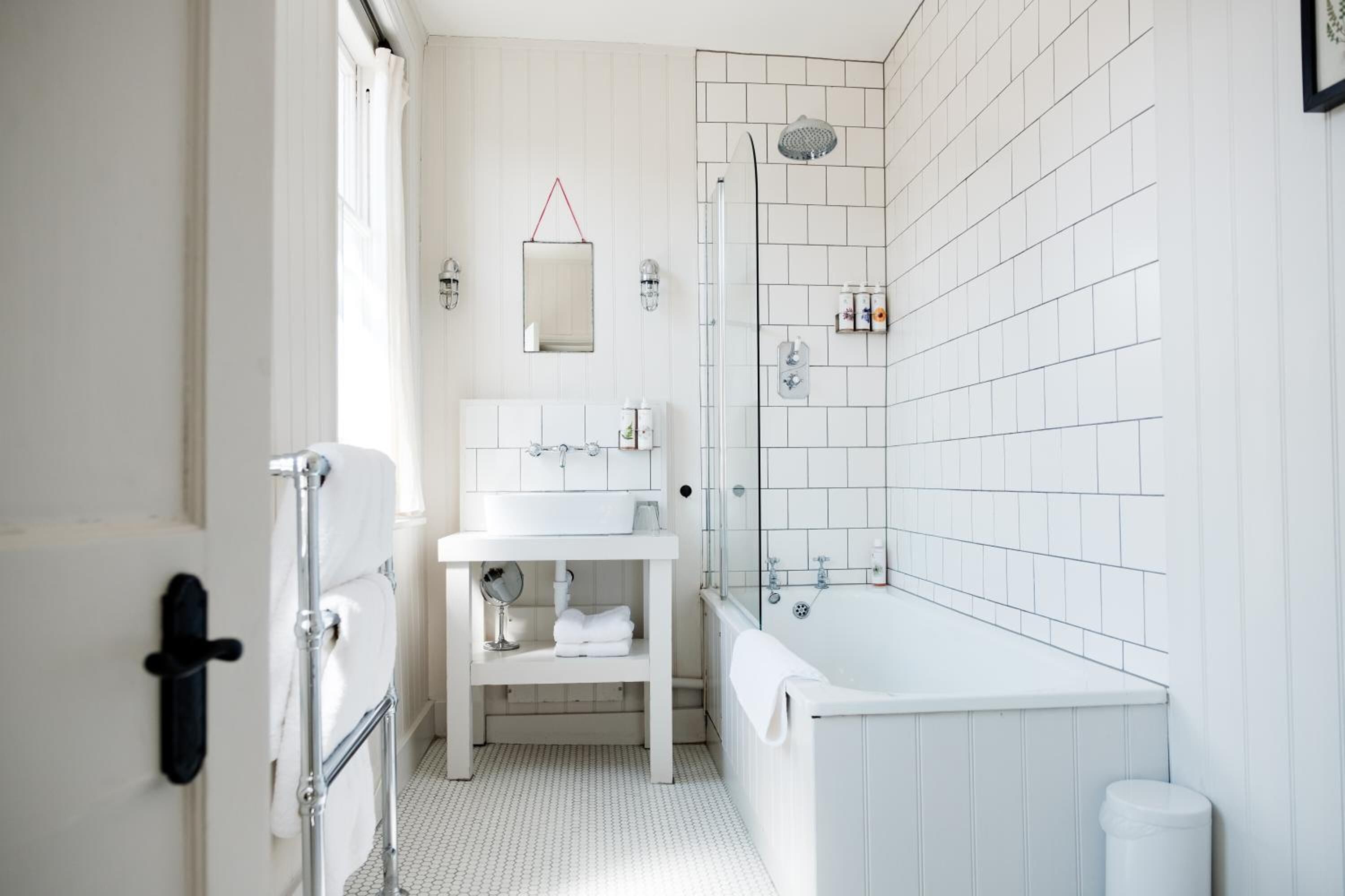 Un baño moderno con azulejos blancos, un lavamanos blanco, una bañera y una cabina de ducha con mampara de vidrio.
