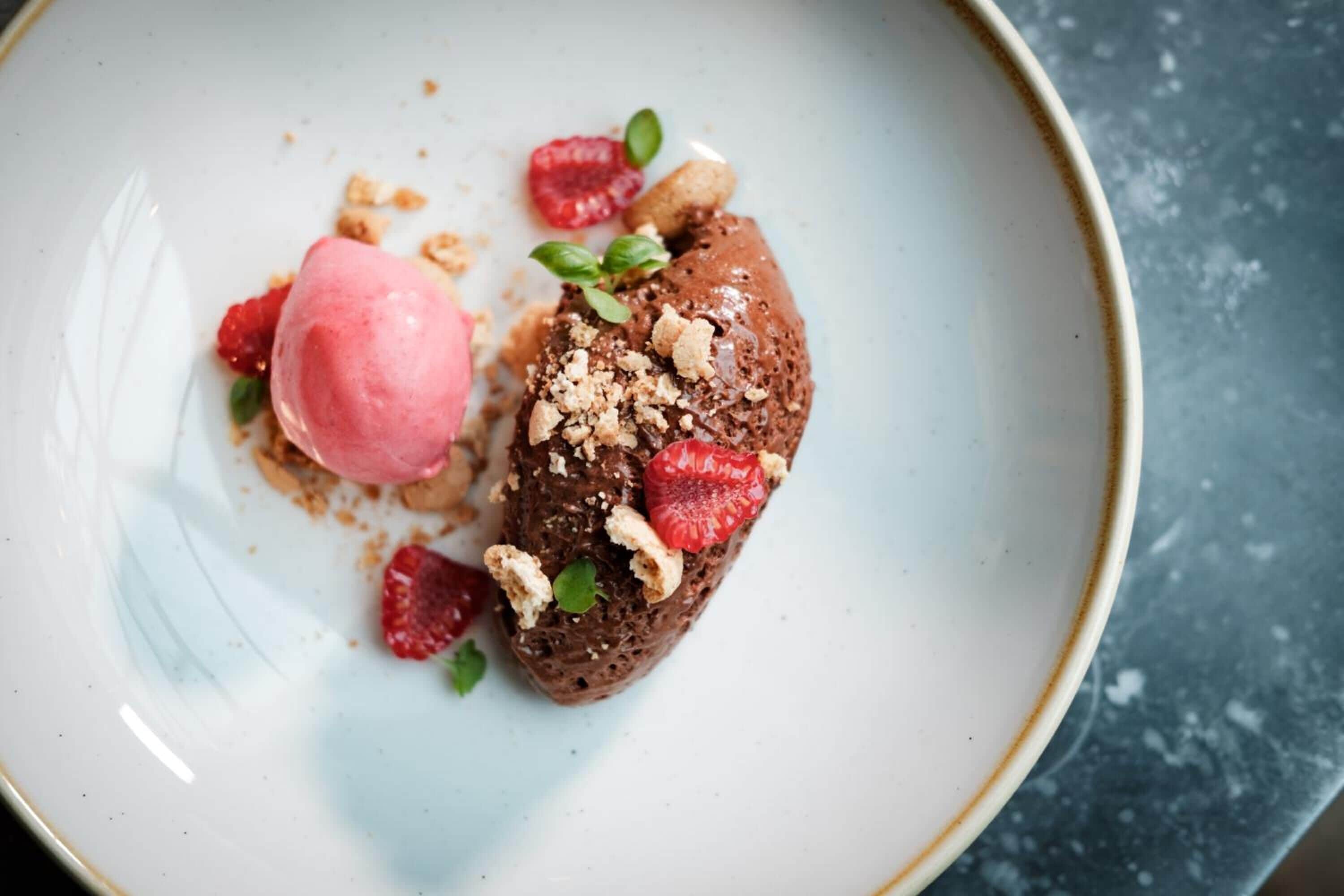 A dessert plate with a chocolate mousse and a scoop of pink ice cream, garnished with raspberries and nuts.