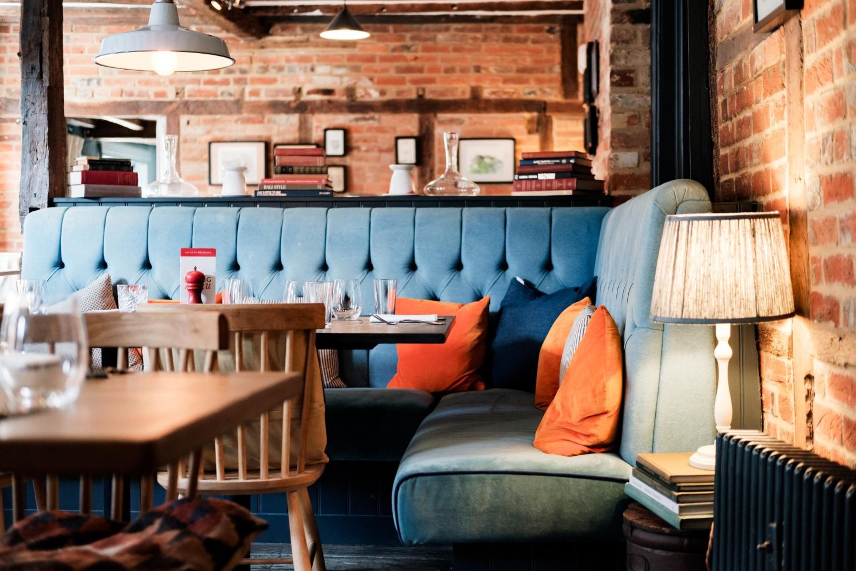 A cozy seating area with a cushioned bench, a table with a lamp, and a brick wall backdrop.