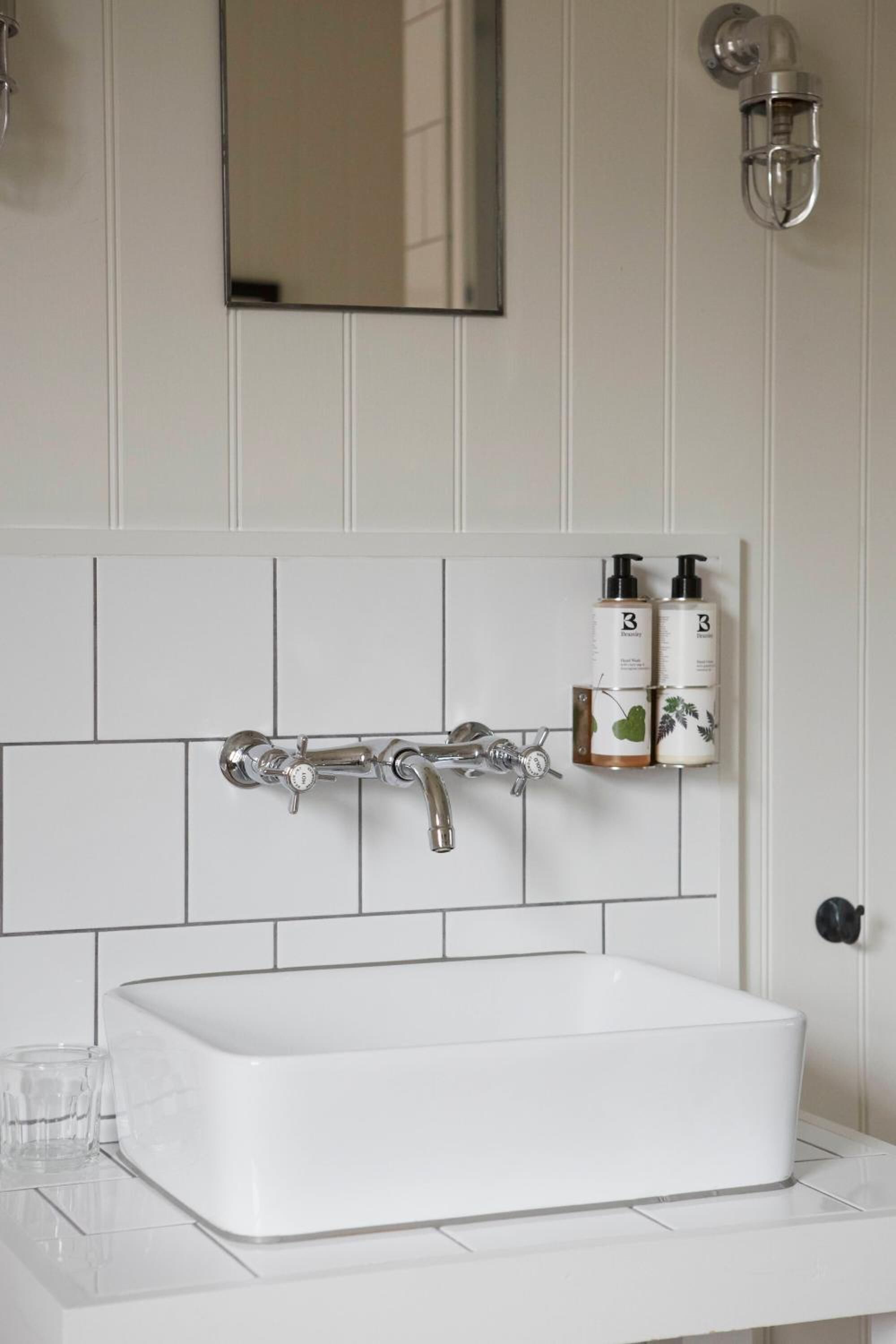 Een badkamer met een wit wastafel, een spiegel erboven en een zeepdispenser op de muur.