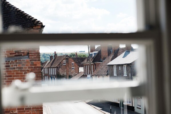 A view through a window of a street with traditional brick buildings, a clear sky, and a road in the foreground. - Bel & The Dragon Kingsclere (Newbury)