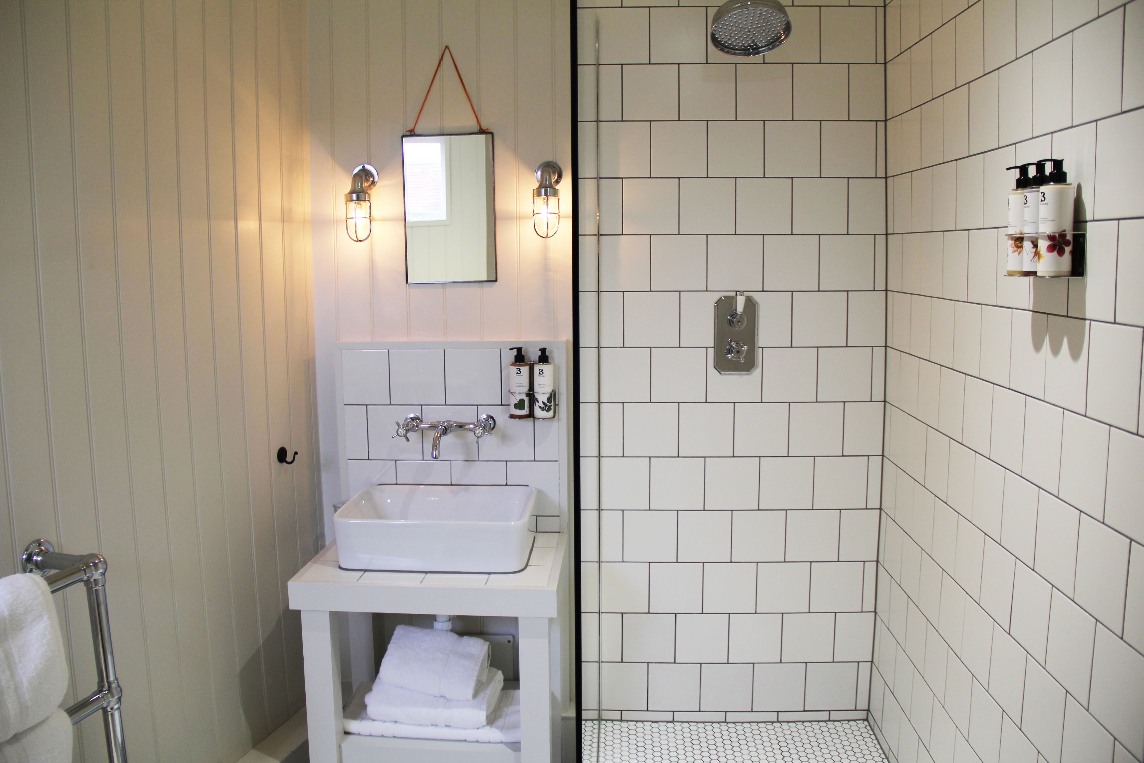 A bathroom with a white sink, mirror, and towel rack. It includes a shower area with tiled walls and a showerhead.