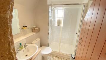 Une salle de bain avec un lavabo blanc, des toilettes et une douche à parois de verre. Un miroir est placé au-dessus du lavabo et une étagère contient des articles de toilette. Le sol est recouvert de carreaux à motifs.
