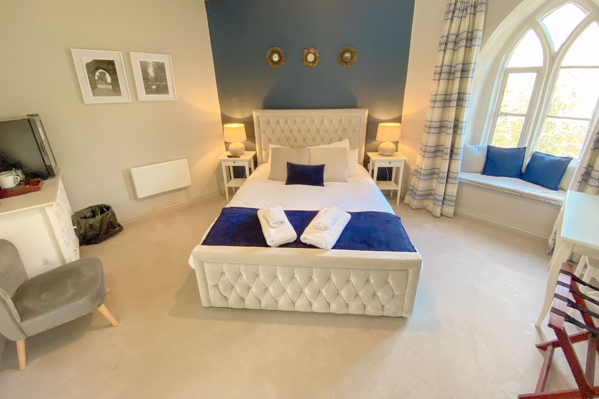 Quarto com uma cama grande, duas mesas de cabeceira, uma cadeira, um assento junto à janela e vista para o exterior.