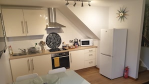 A compact kitchen with white cabinets, a microwave, a stove, and a refrigerator. - Bancroft Apartment (Durham)