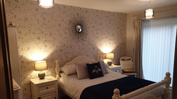 A bedroom with a bed, two bedside tables, a mirror, and a window with curtains. - Bancroft Apartment (Durham)