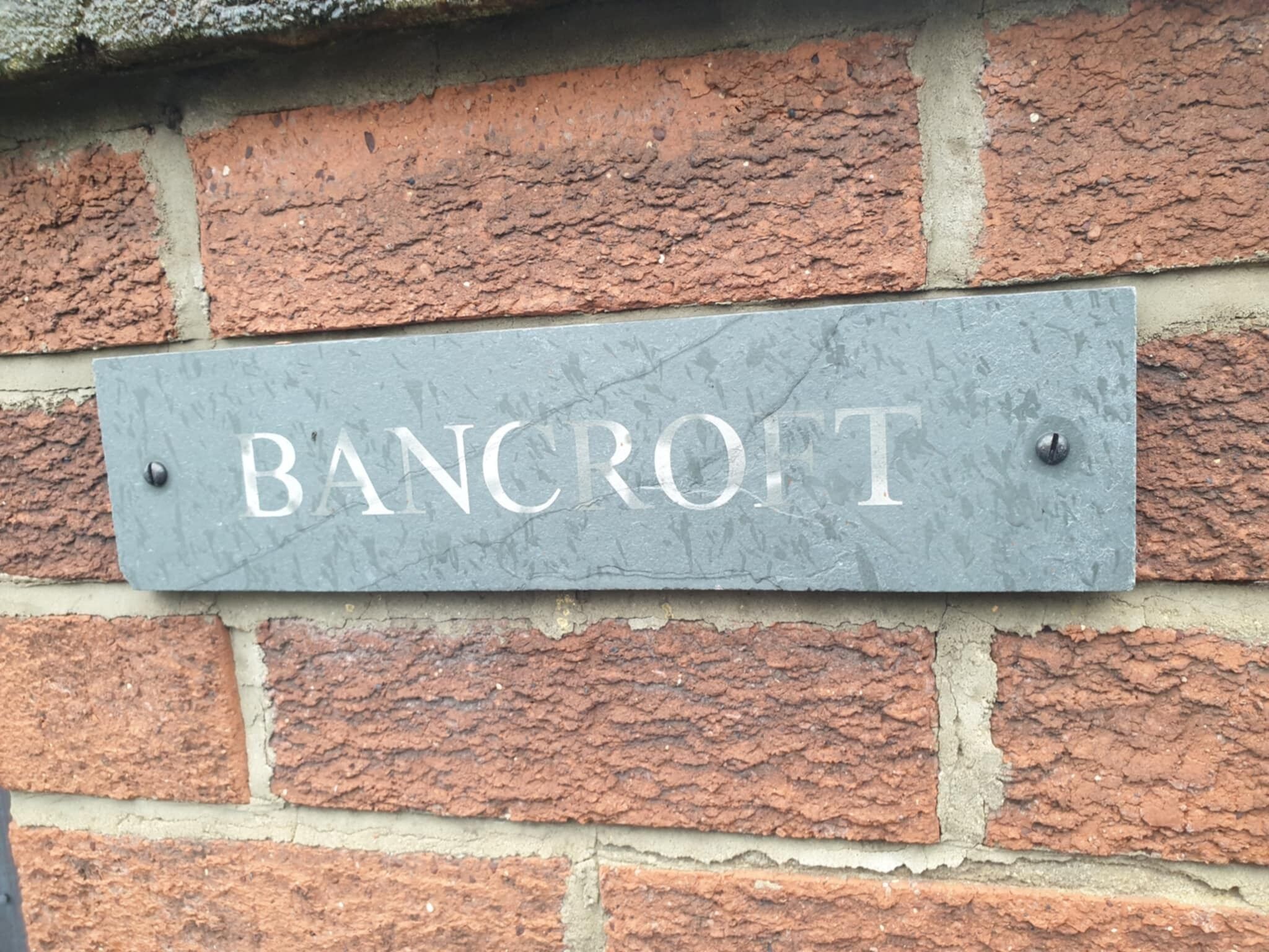Un cartello di metallo grigio con la scritta 'BANCRIFT' incisa, fissato a un muro di mattoni.