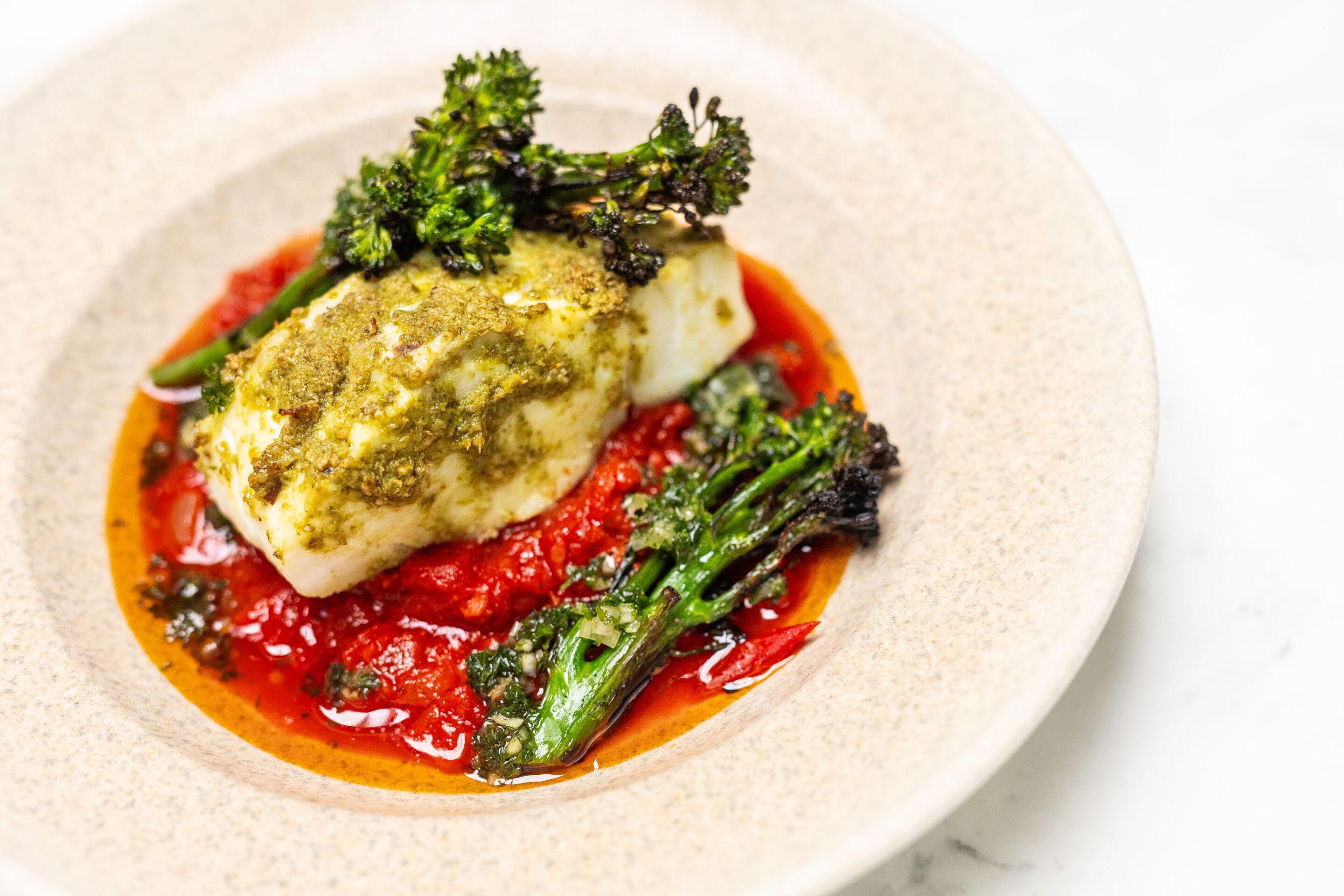 A plate with a piece of white fish, green vegetables, and a red sauce.