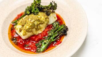 A plate with a piece of white fish, green vegetables, and a red sauce.