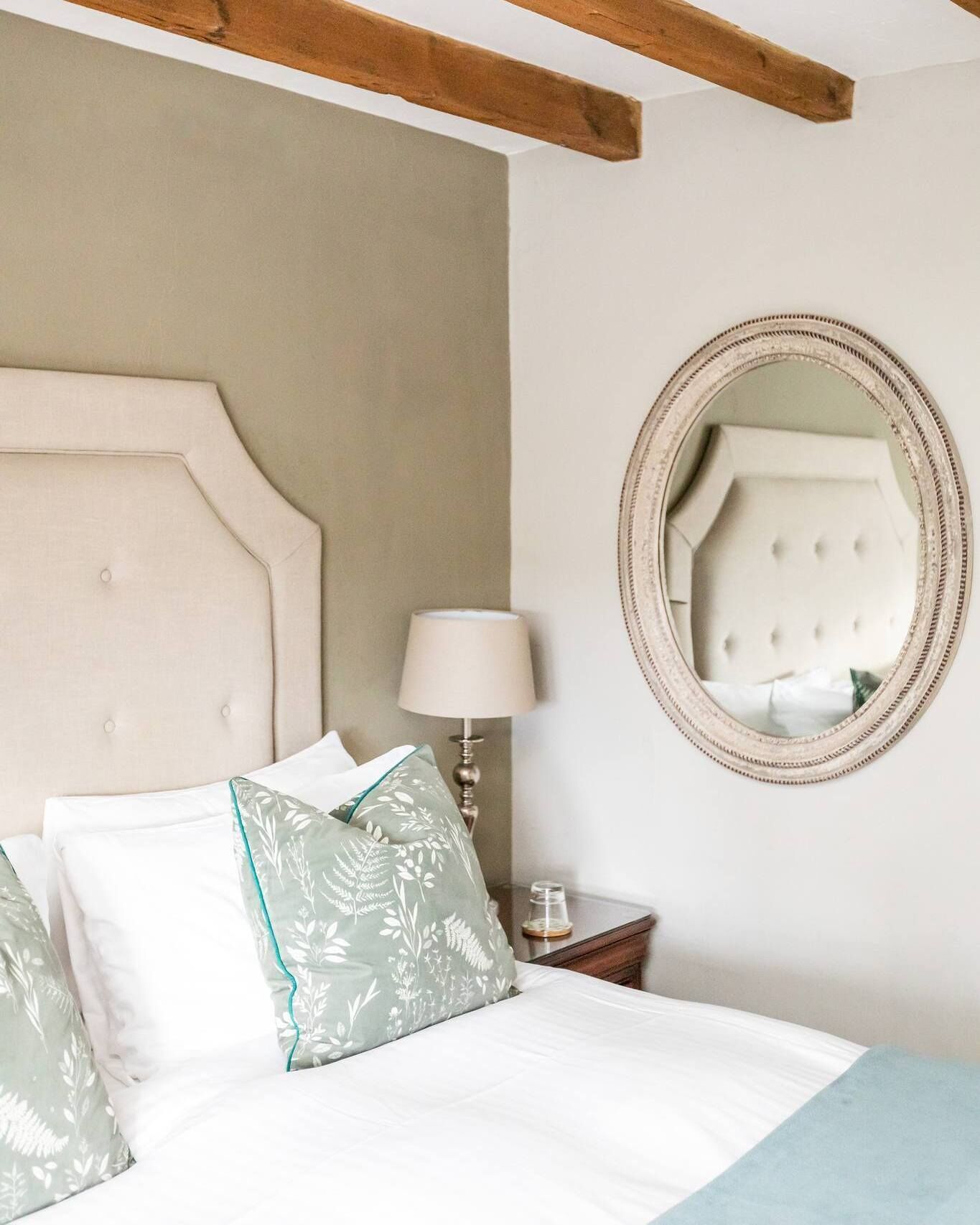 A bedroom with a large bed, a round mirror, and a nightstand with a lamp.