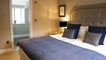 A bedroom with a large bed, a nightstand with a lamp, and a framed picture on the wall.
