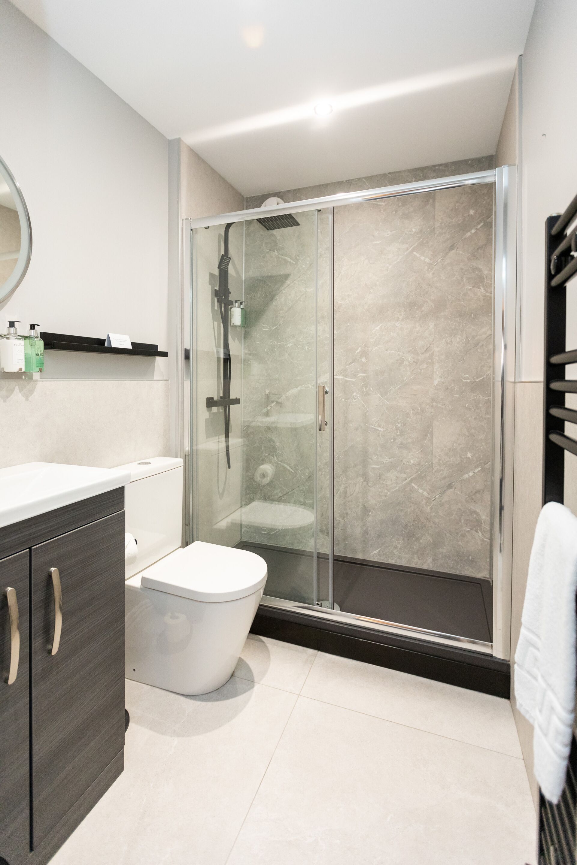 Un baño moderno con ducha envuelta en vidrio, inodoro blanco y tocador de madera oscura.
