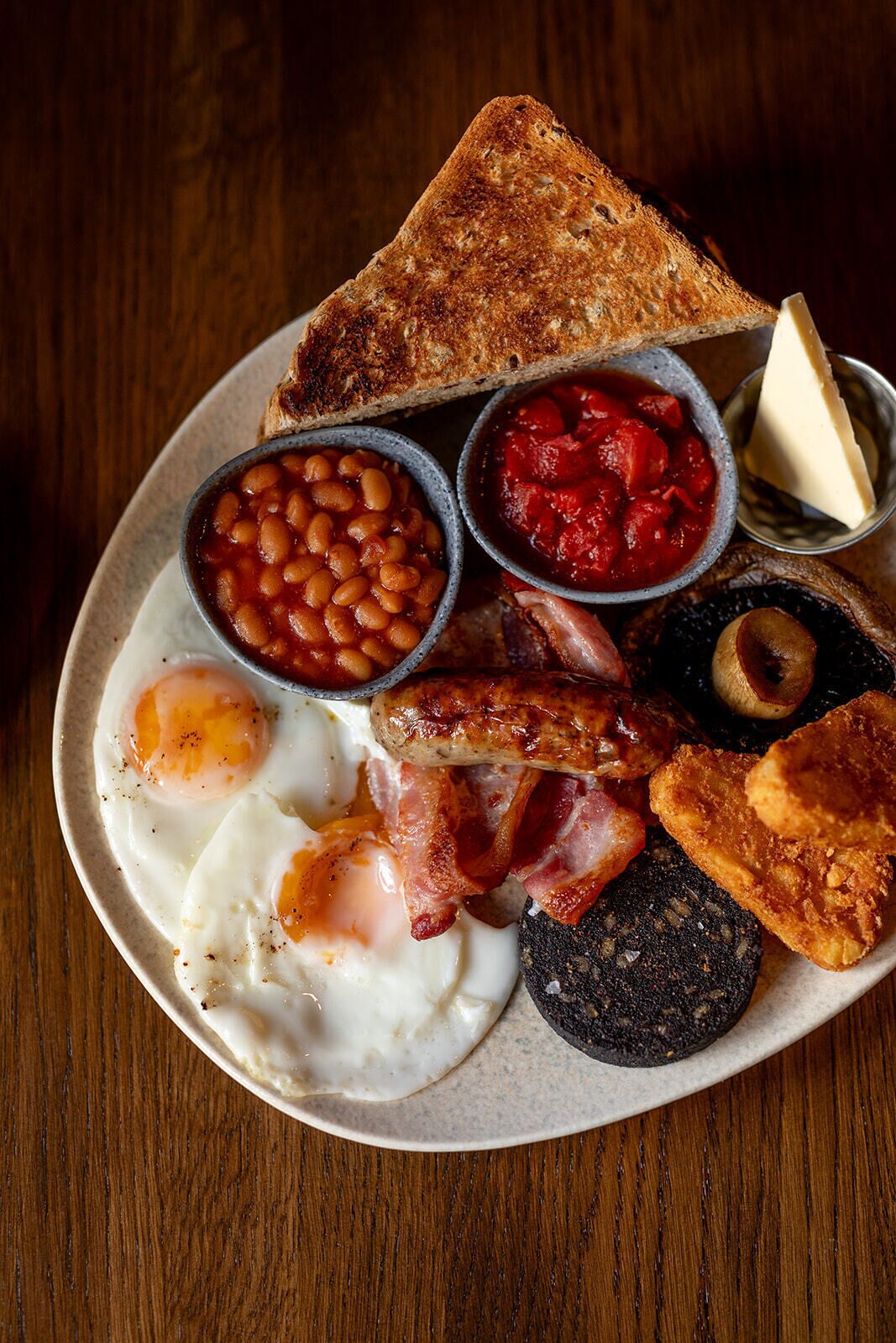 A plate of breakfast food including eggs, sausages, bacon, toast, beans, and tomato sauce.