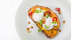 A plate with a slice of toast topped with poached eggs, microgreens, and red pepper slices. - The Dragon (Derby)