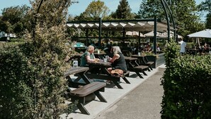 An outdoor seating area with tables and benches under a covered structure. - The Dragon (Derby)