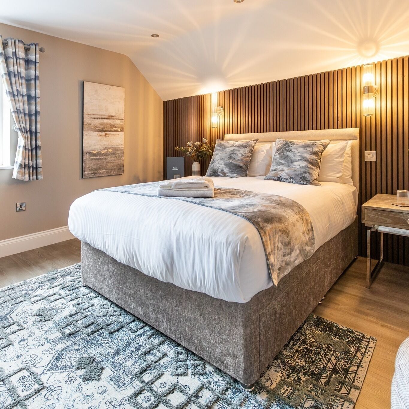 Un dormitorio moderno con una cama grande, un cabecero de madera, una mesita de noche y una lámpara de pared.