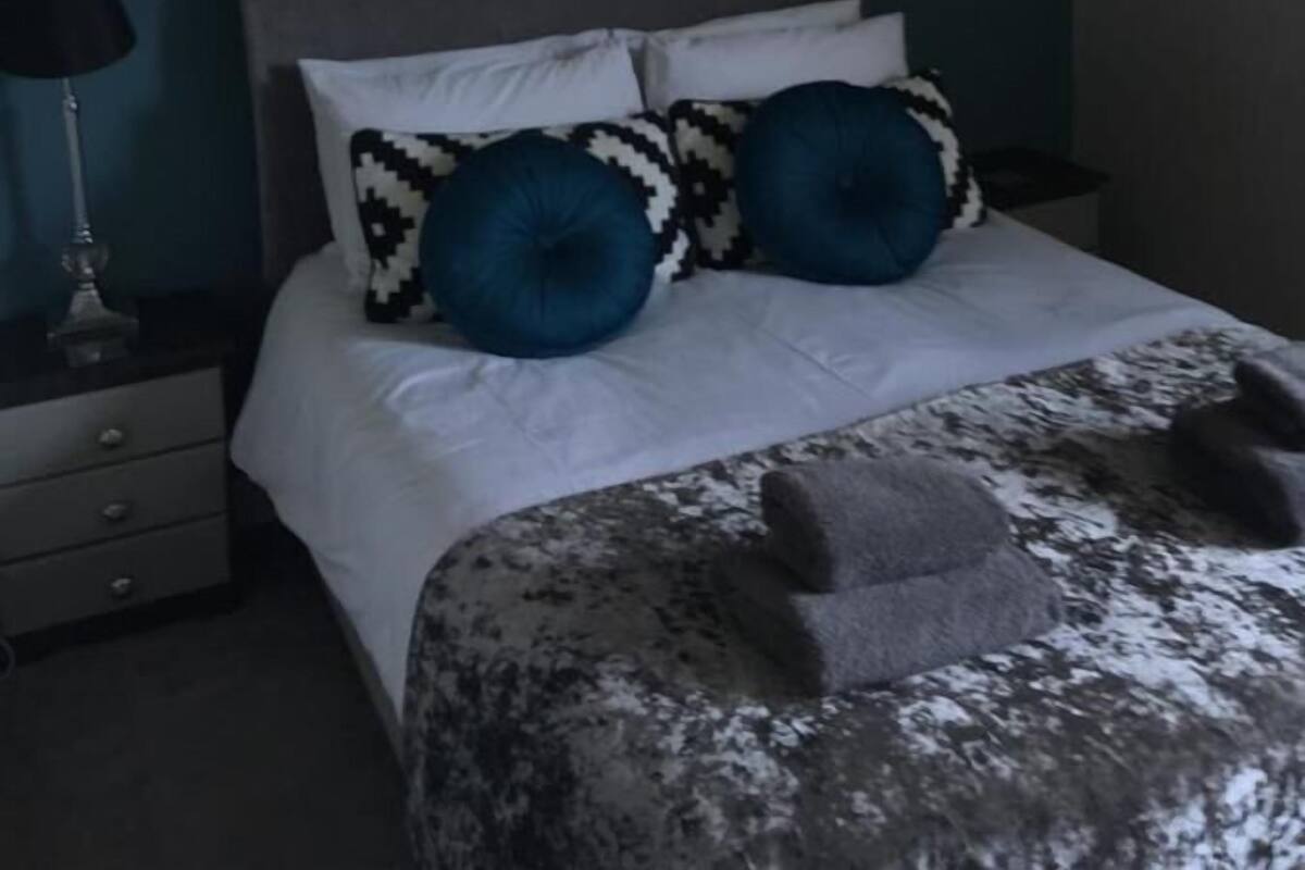 Un dormitorio con cama, candelabro, un cuadro en la pared y mesita de noche con lámpara.