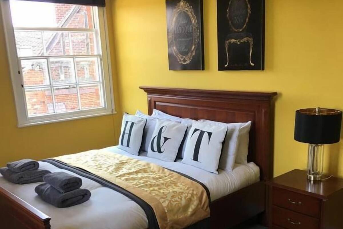 Un dormitorio con una cama, ventana, lámpara y cómoda.