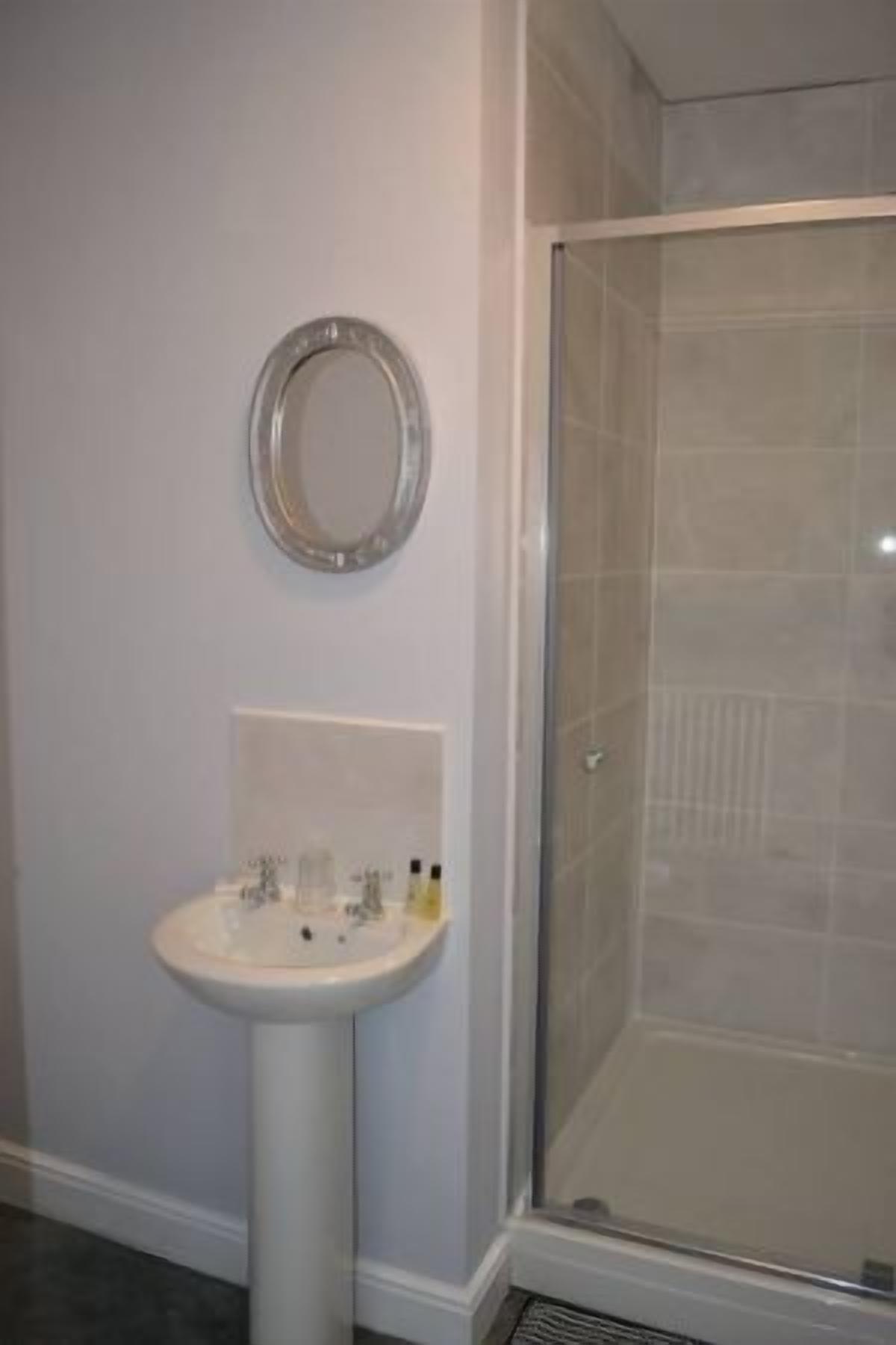 A bathroom with a pedestal sink, a mirror, and a glass shower enclosure.