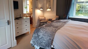 A bedroom with a bed, a dresser, a chair, a mirror, and a window with curtains. - Boscastle House (Boscastle)