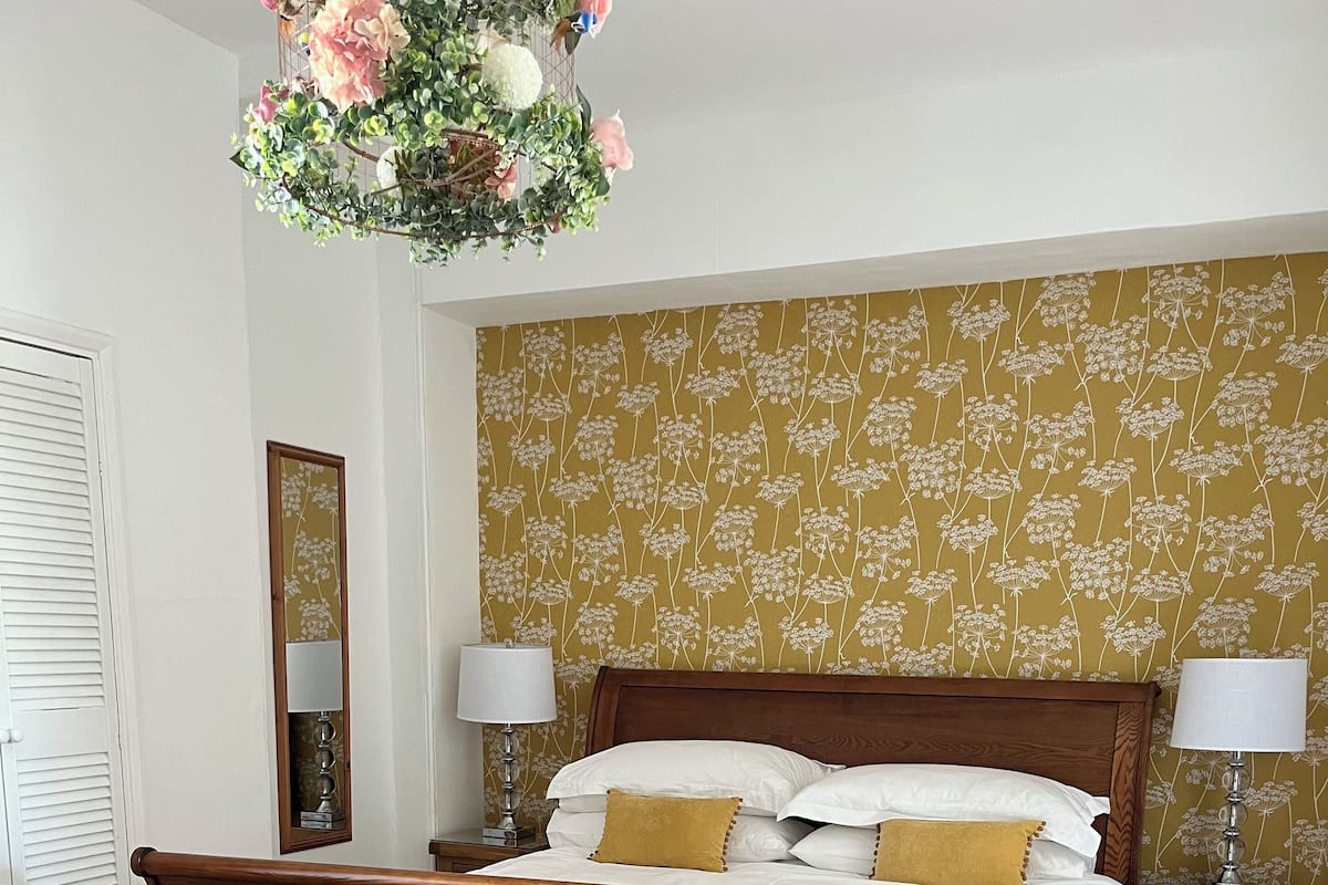A bedroom with a wooden bed, two bedside tables, a mirror, and a floral-patterned wallpaper.