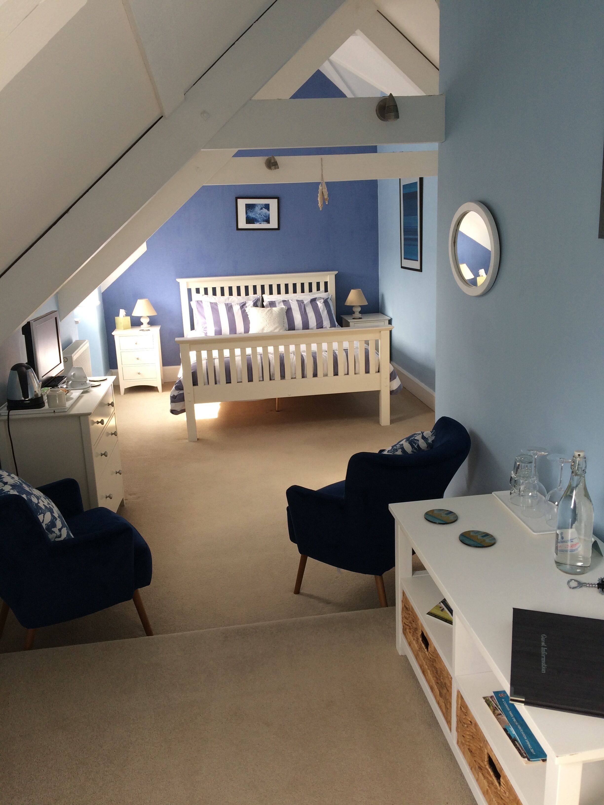 A bedroom with a white bed, a desk with a computer, a chair, and a small table with decorative items.