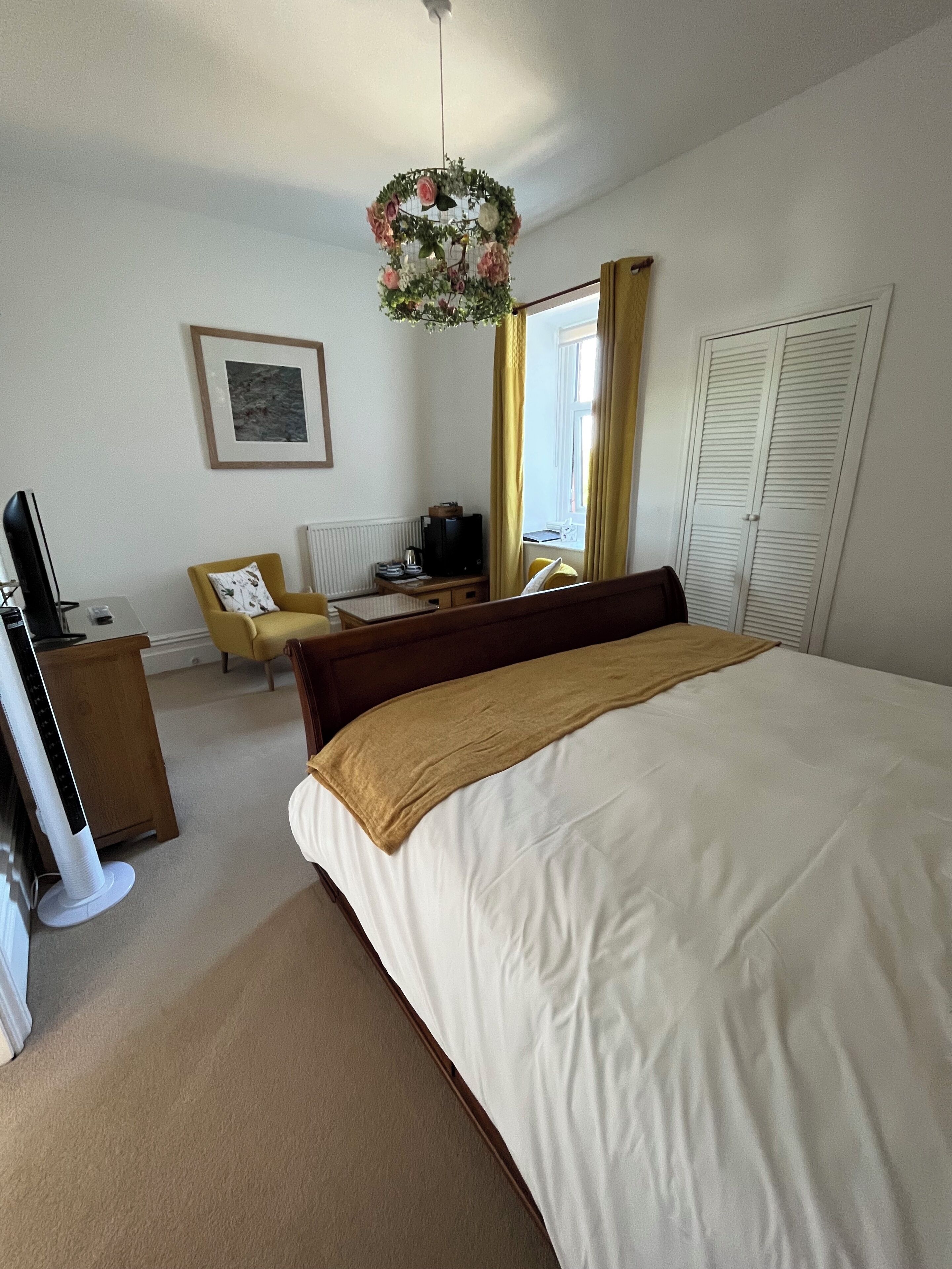 A neatly arranged bedroom with a large bed, a desk, a chair, and a television.