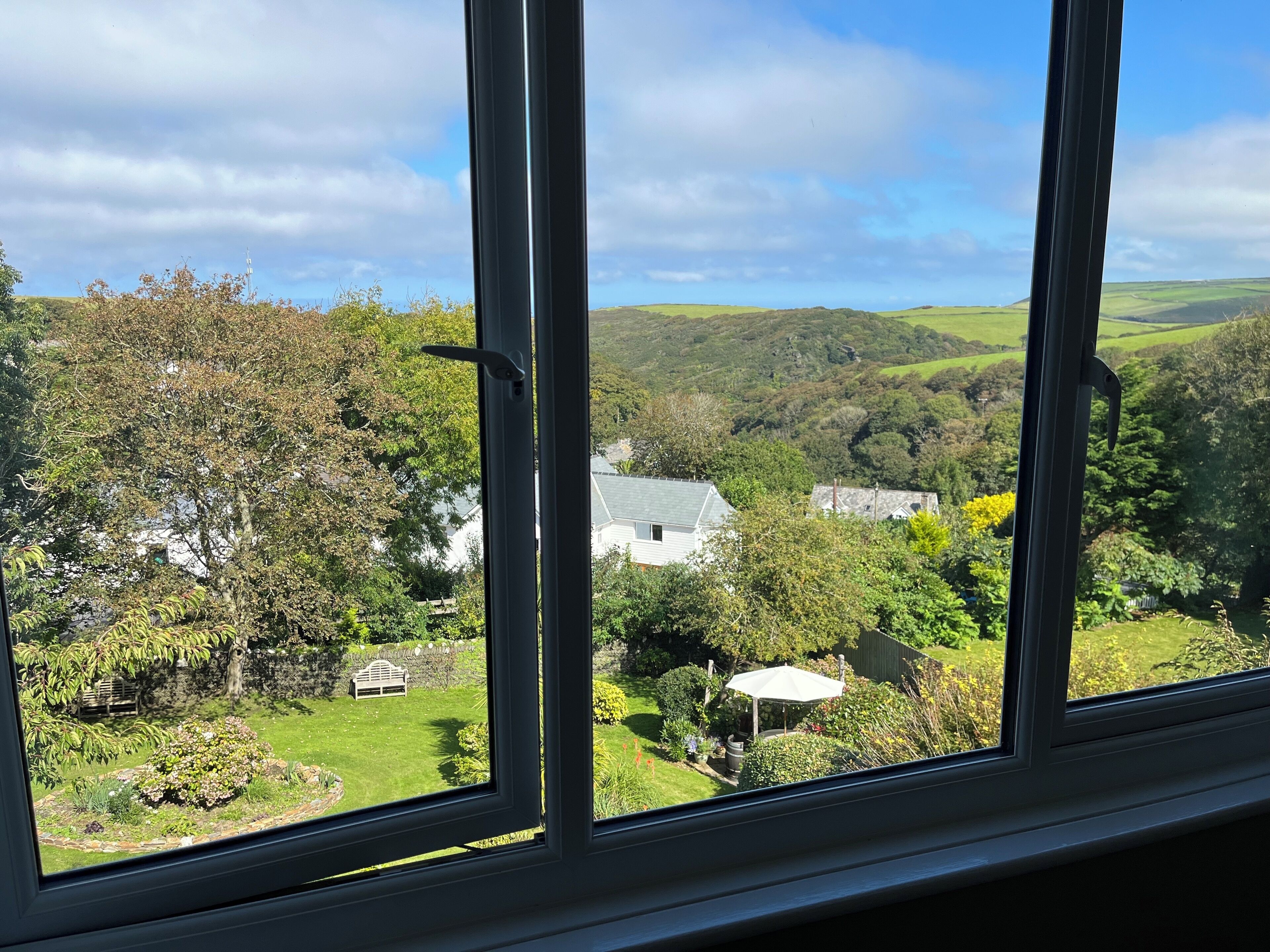 A view through a window of a house surrounded by lush greenery and rolling hills.