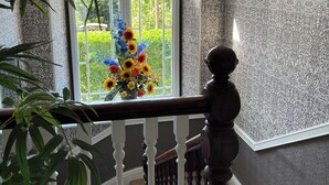 A staircase with a patterned wall, a chandelier, and a window with a floral arrangement. - Boscastle House (Boscastle)
