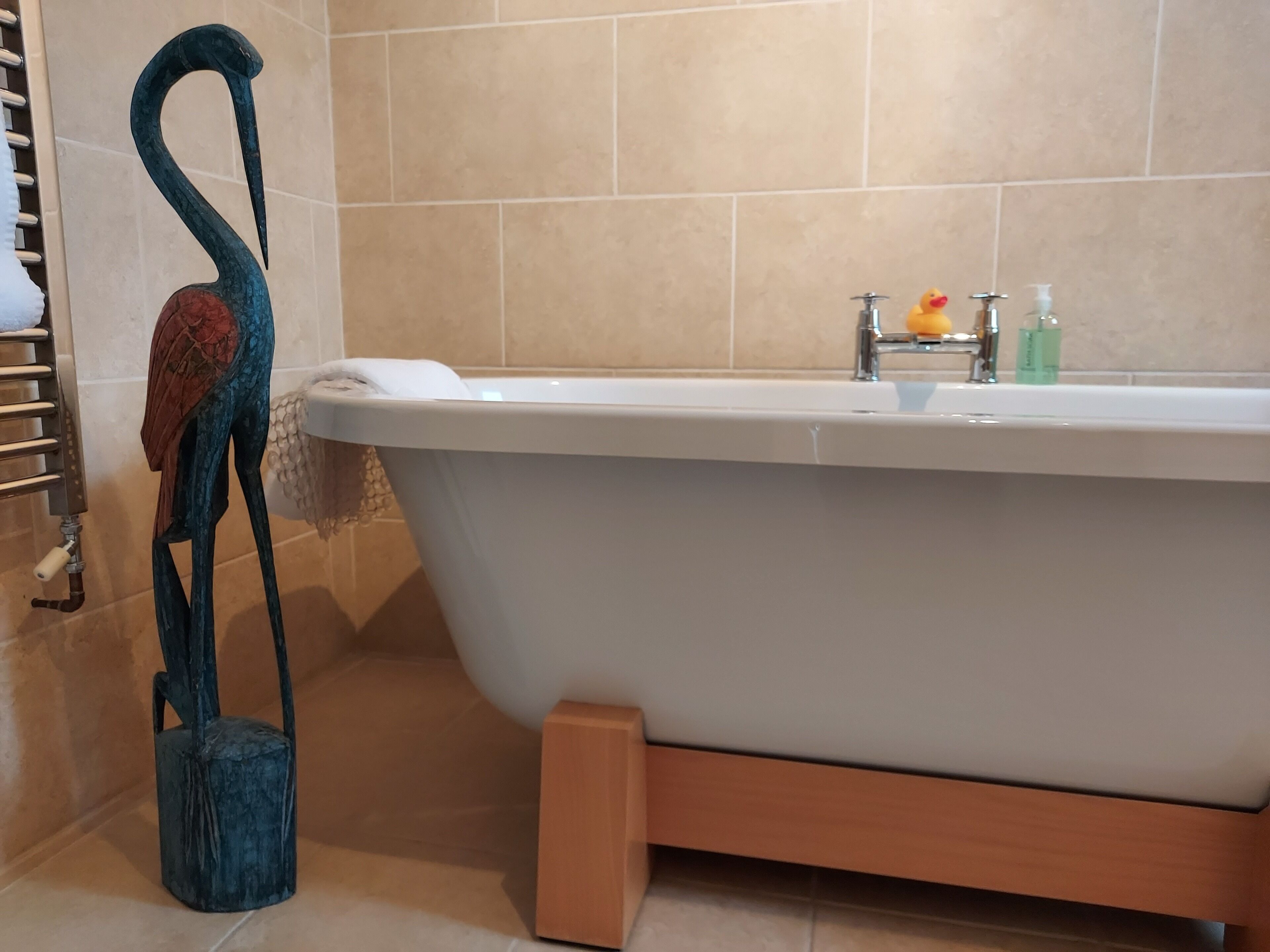 A bathroom with a freestanding bathtub, a towel rack, and a decorative sculpture.