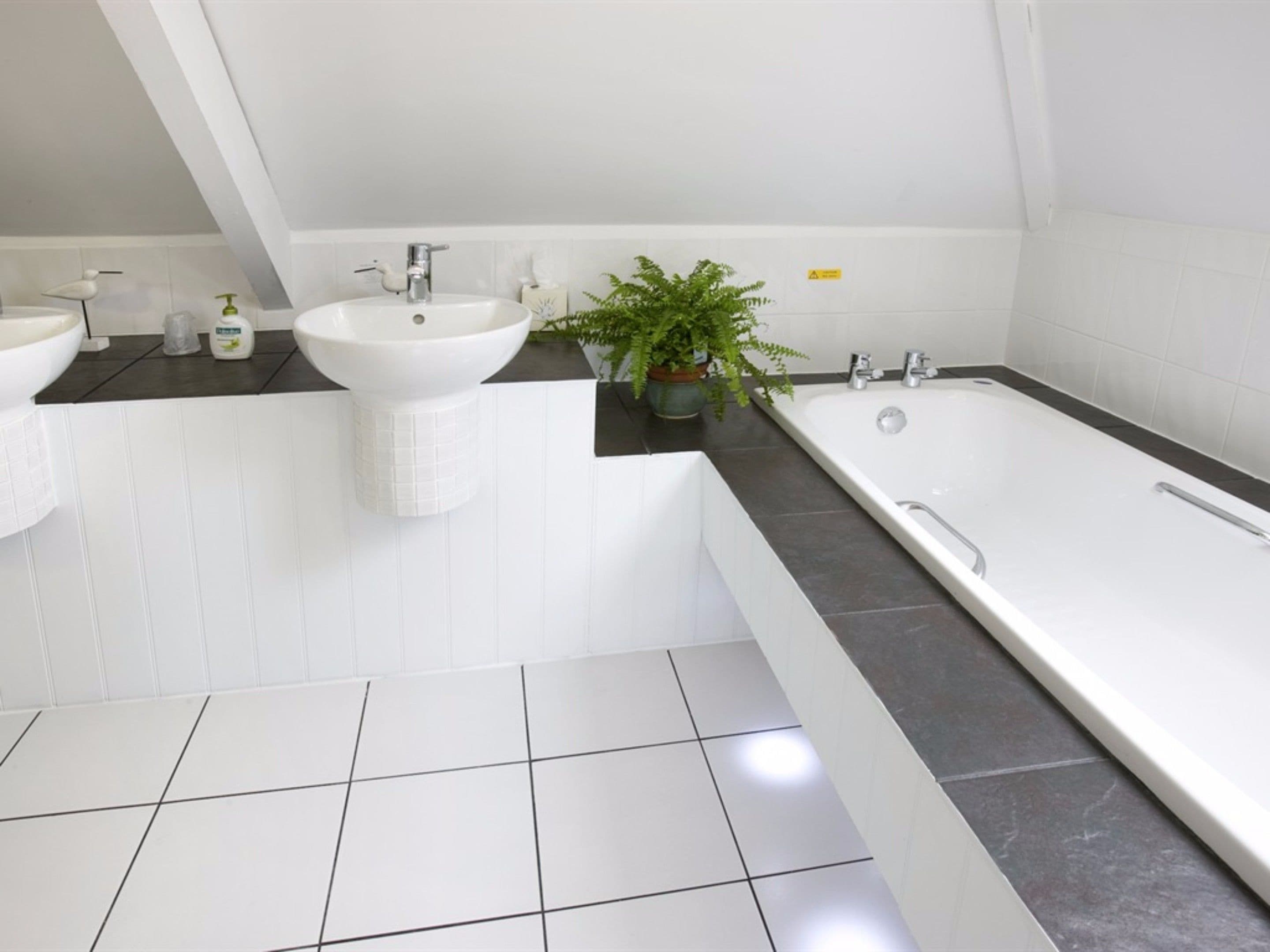 Un baño moderno con dos lavamanos, una bañera y una planta en maceta.