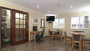 A room with a wooden door, a television mounted on the wall, a dining table with chairs, and a window with blinds. - Valley Inn Shakopee (Shakopee)