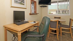 A room with a wooden desk, a computer, a chair, a television mounted on the wall, and a window with blinds. - Valley Inn Shakopee (Shakopee)